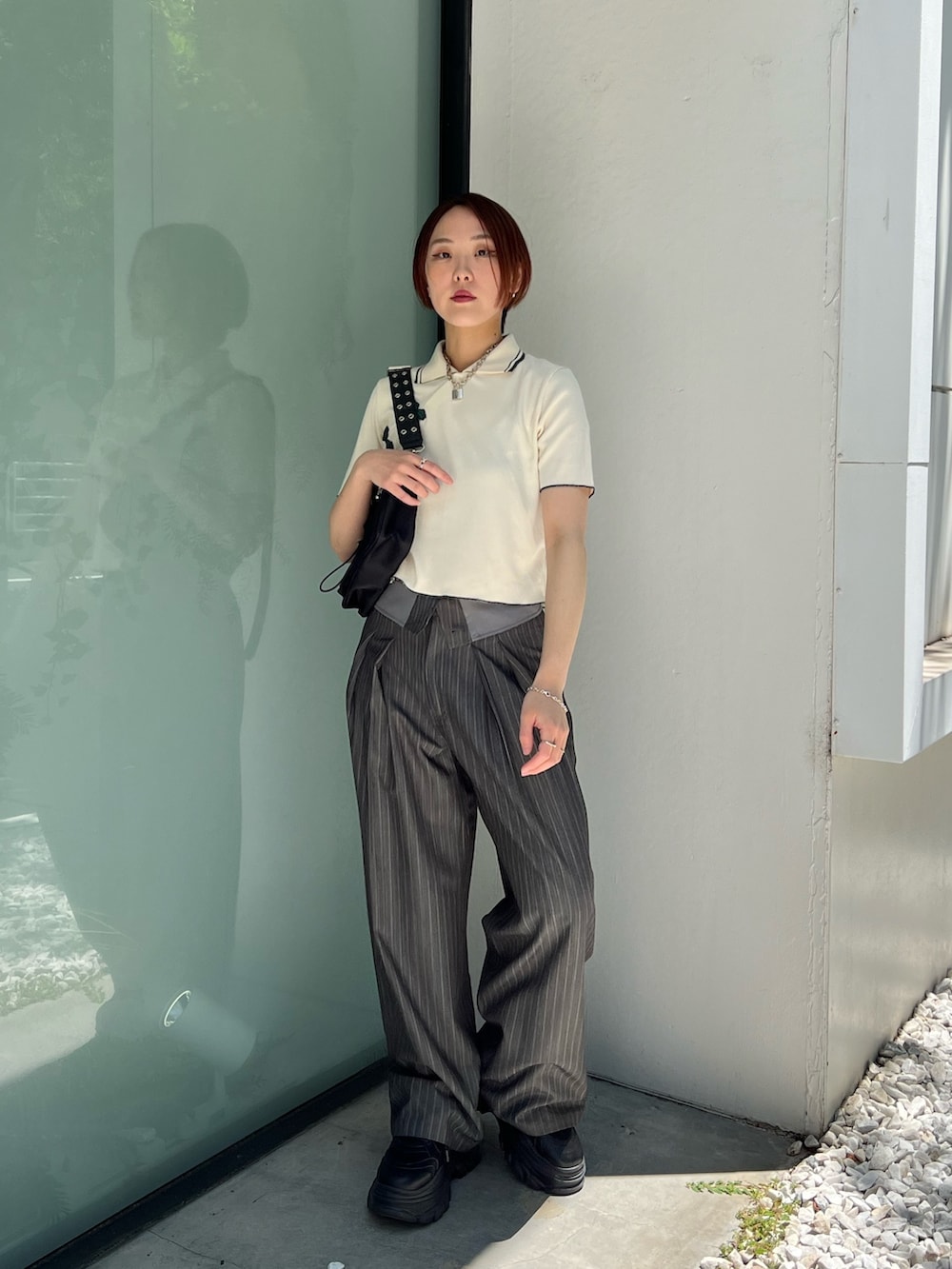ホワイト系のポロシャツ、グレー系のスラックス、ブラック系のショルダーバッグを着用したレディースの夏コーディネートの2枚目の写真