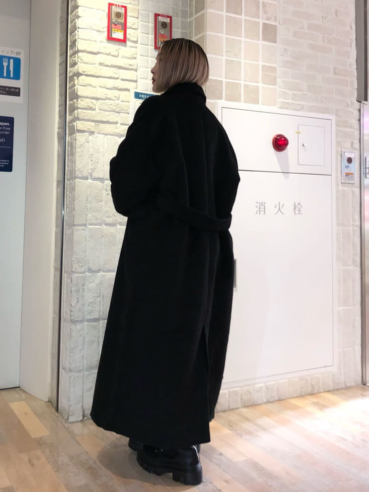 ブラック系のチェスターコート、レッド系のニット/セーター、ブラック系のブーツを着用したレディースの冬コーディネートの3枚目の写真