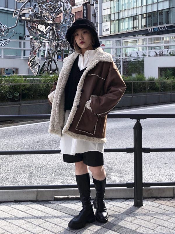 ブラウン系のムートンコート、ブラック系のシャツワンピース、ブラック系のハットを着用したレディースの秋コーディネートの2枚目の写真