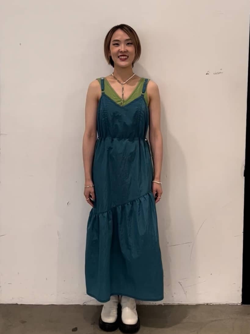 ホワイト系のブーツ、ブルー系のジャンパースカート、グリーン系のキャミソールを着用したレディースの秋コーディネートの2枚目の写真