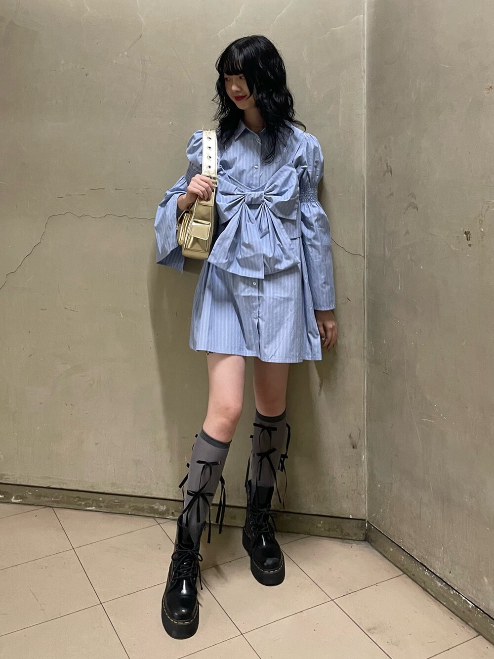 ブルー系のシャツワンピース、ゴールド系のハンドバッグ、ブラック系のブーツを着用したレディースの夏コーディネートの2枚目の写真
