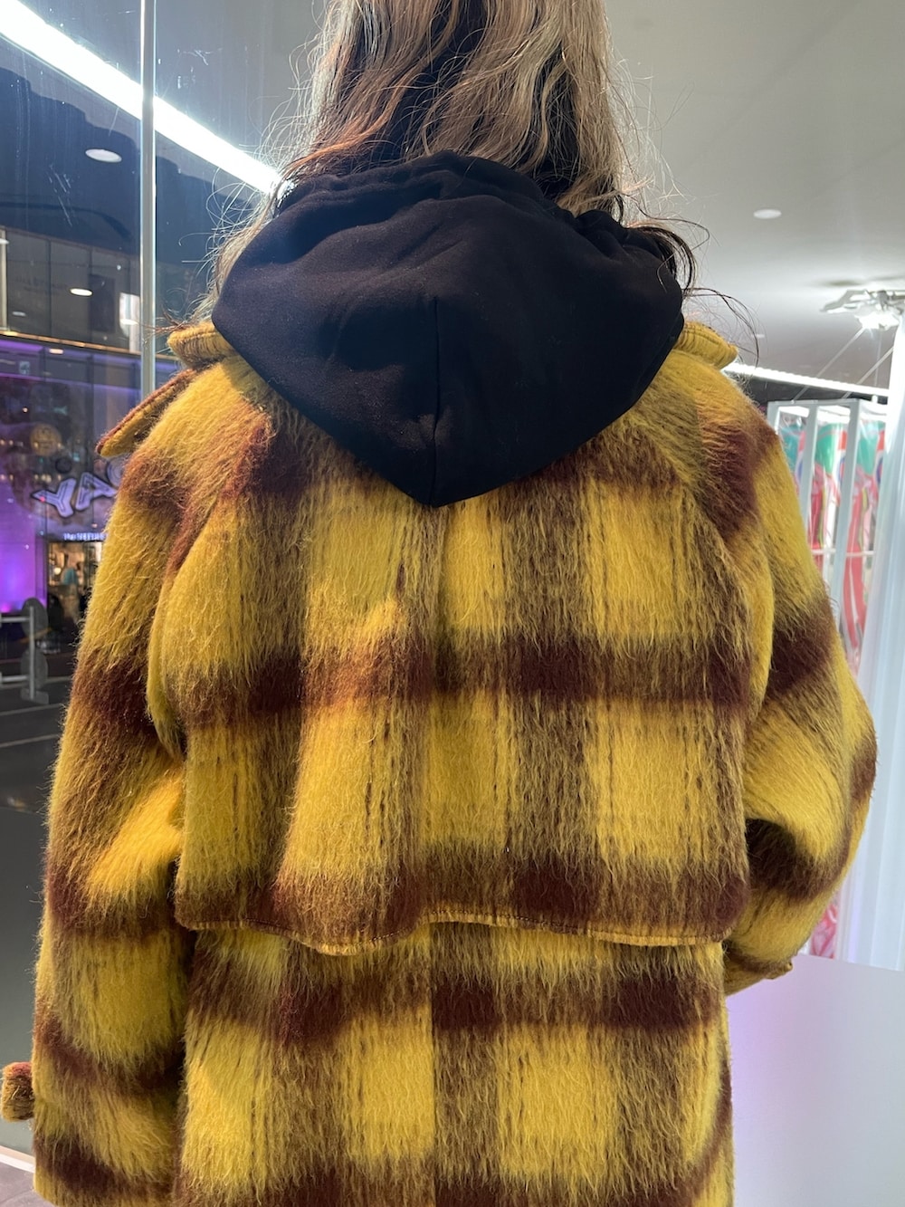 イエロー系のチェスターコート、ブラック系のパーカー、ブラック系のショルダーバッグを着用したレディースの冬コーディネートの8枚目の写真