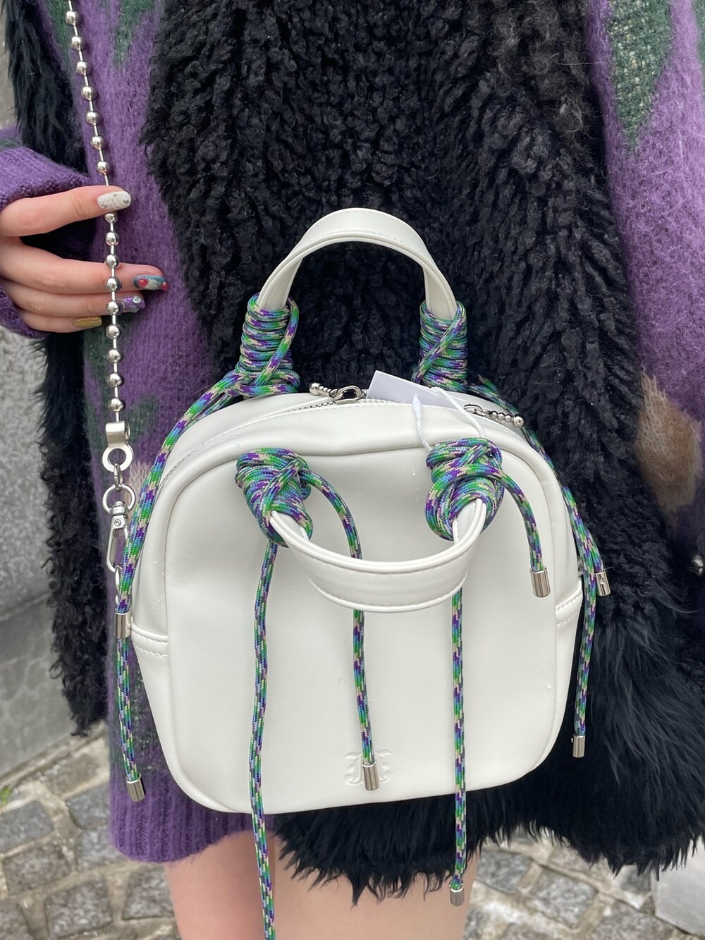 パープル系のニット/セーター、ホワイト系のショルダーバッグ、ブラック系のベストを着用したレディースの冬コーディネートの7枚目の写真