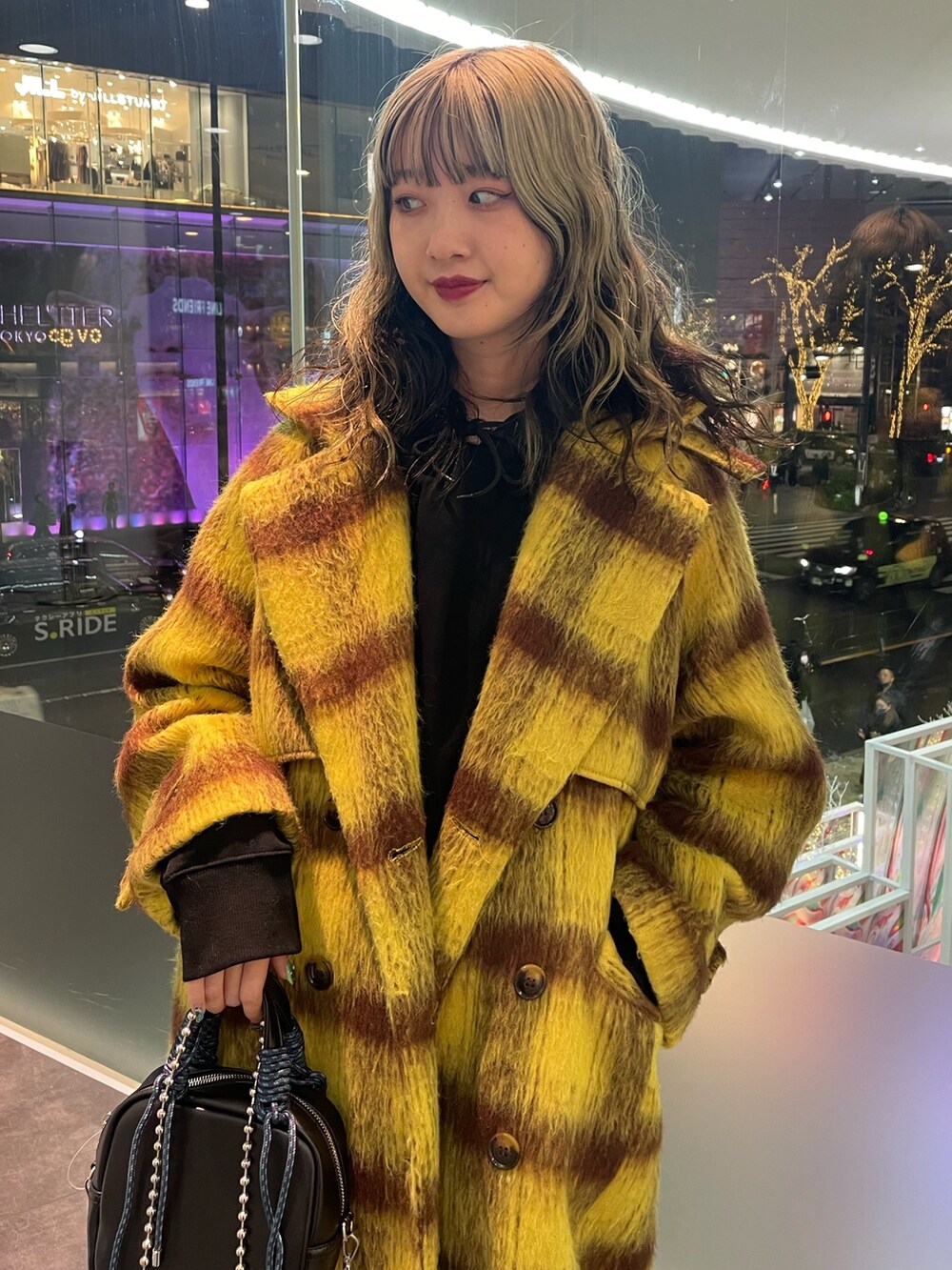 イエロー系のチェスターコート、ブラック系のパーカー、ブラック系のショルダーバッグを着用したレディースの冬コーディネートの4枚目の写真