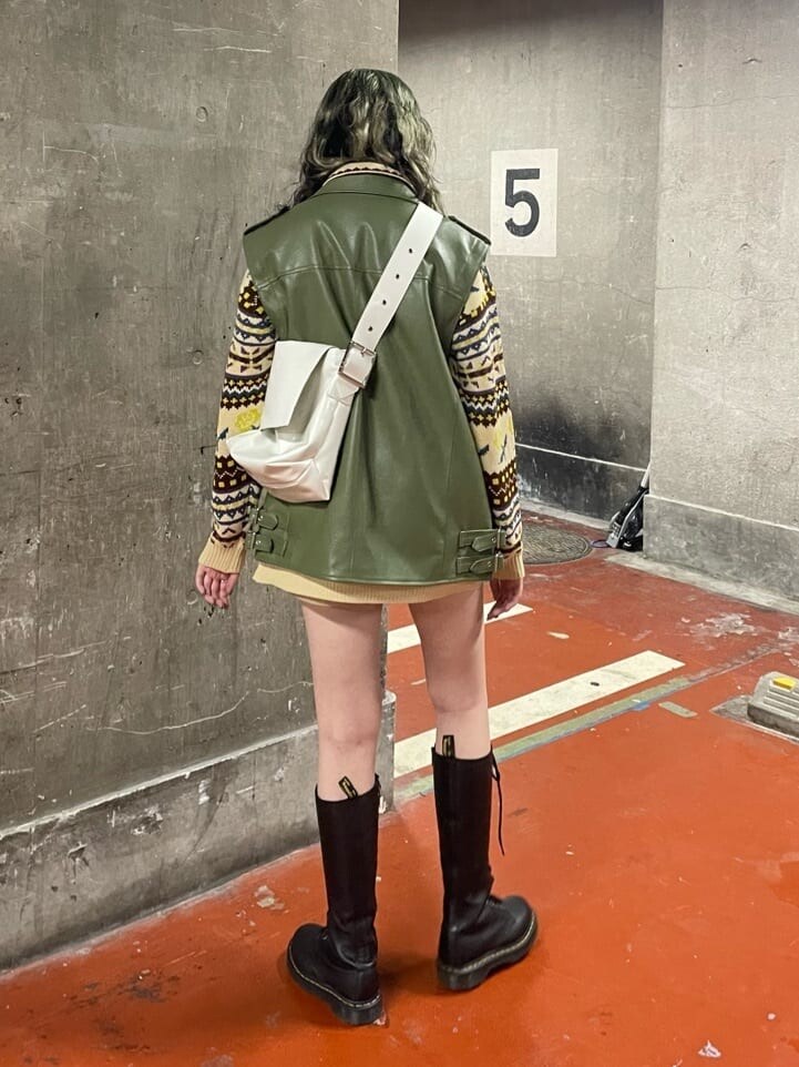 ブラック系のブーツ、ホワイト系のハンドバッグ、グリーン系のライダースジャケットを着用したレディースの秋コーディネートの3枚目の写真