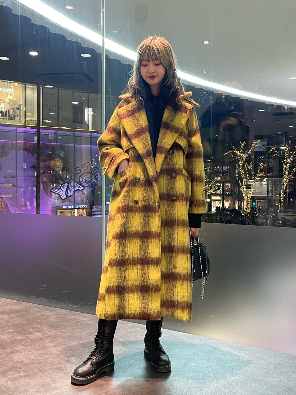 イエロー系のチェスターコート、ブラック系のパーカー、ブラック系のショルダーバッグを着用したレディースの冬コーディネートの2枚目の写真