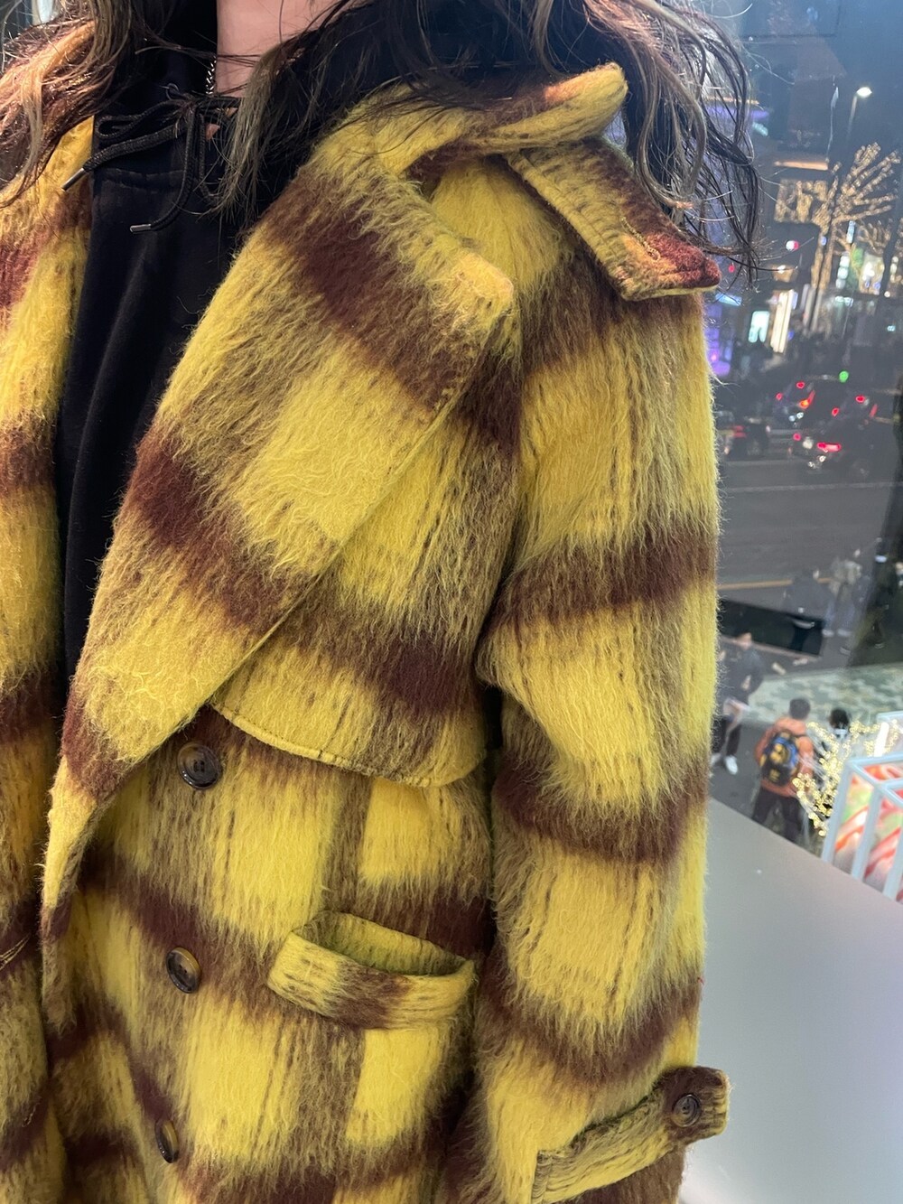 イエロー系のチェスターコート、ブラック系のパーカー、ブラック系のショルダーバッグを着用したレディースの冬コーディネートの7枚目の写真