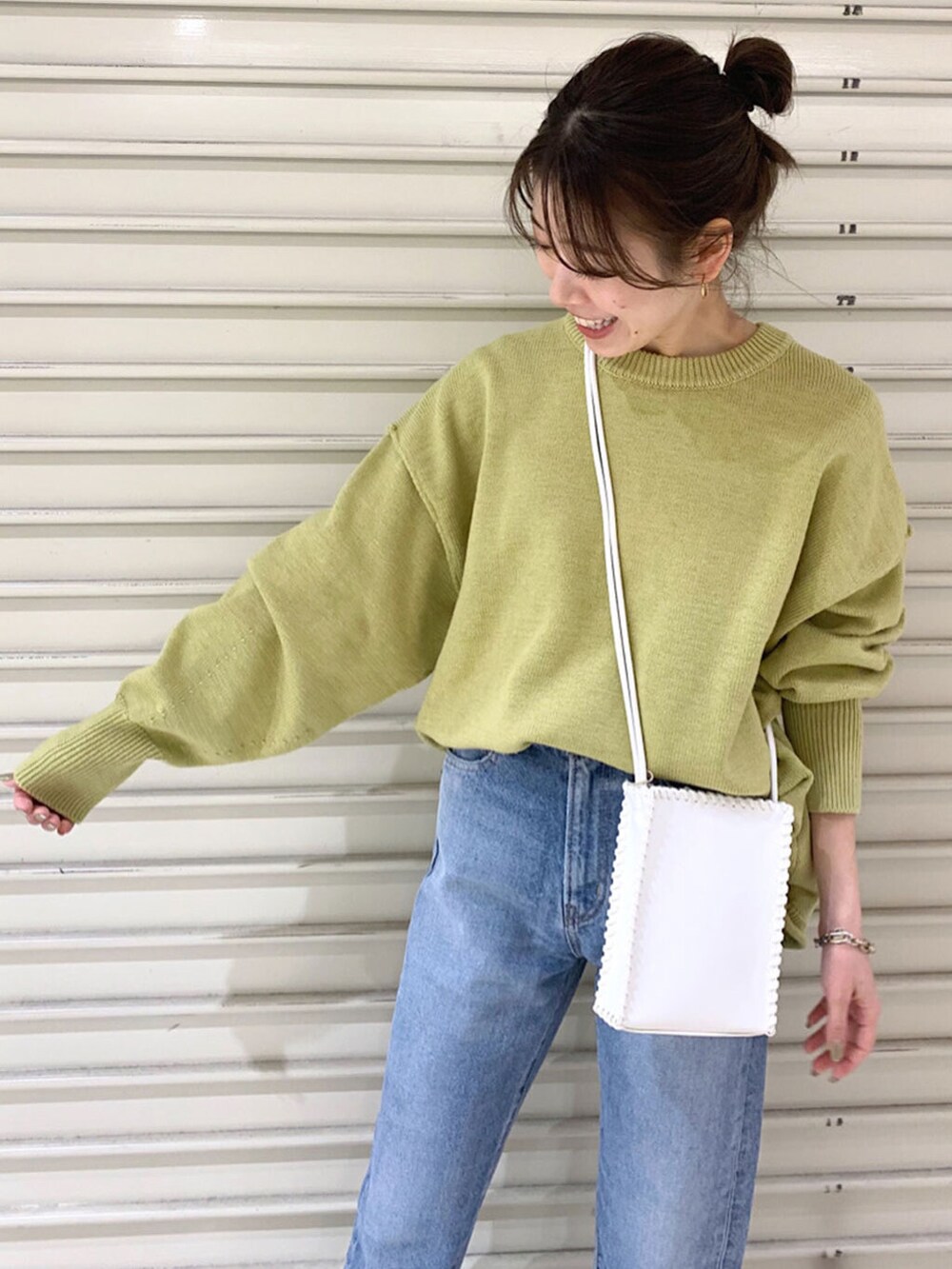 ブルー系のデニムパンツ、ホワイト系のショルダーバッグ、グリーン系のニット/セーターを着用したレディースの冬コーディネートの4枚目の写真