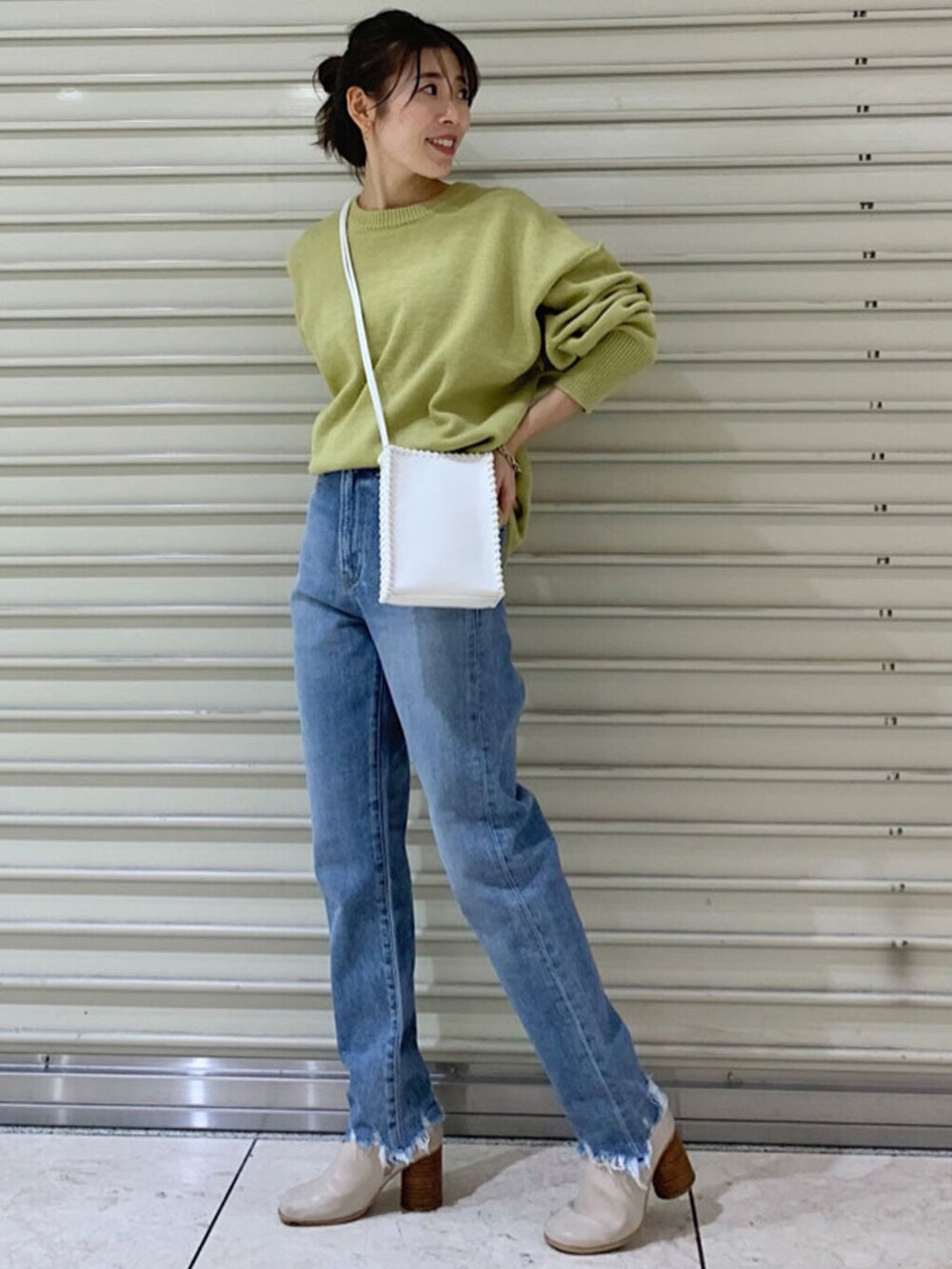 ブルー系のデニムパンツ、ホワイト系のショルダーバッグ、グリーン系のニット/セーターを着用したレディースの冬コーディネートの3枚目の写真