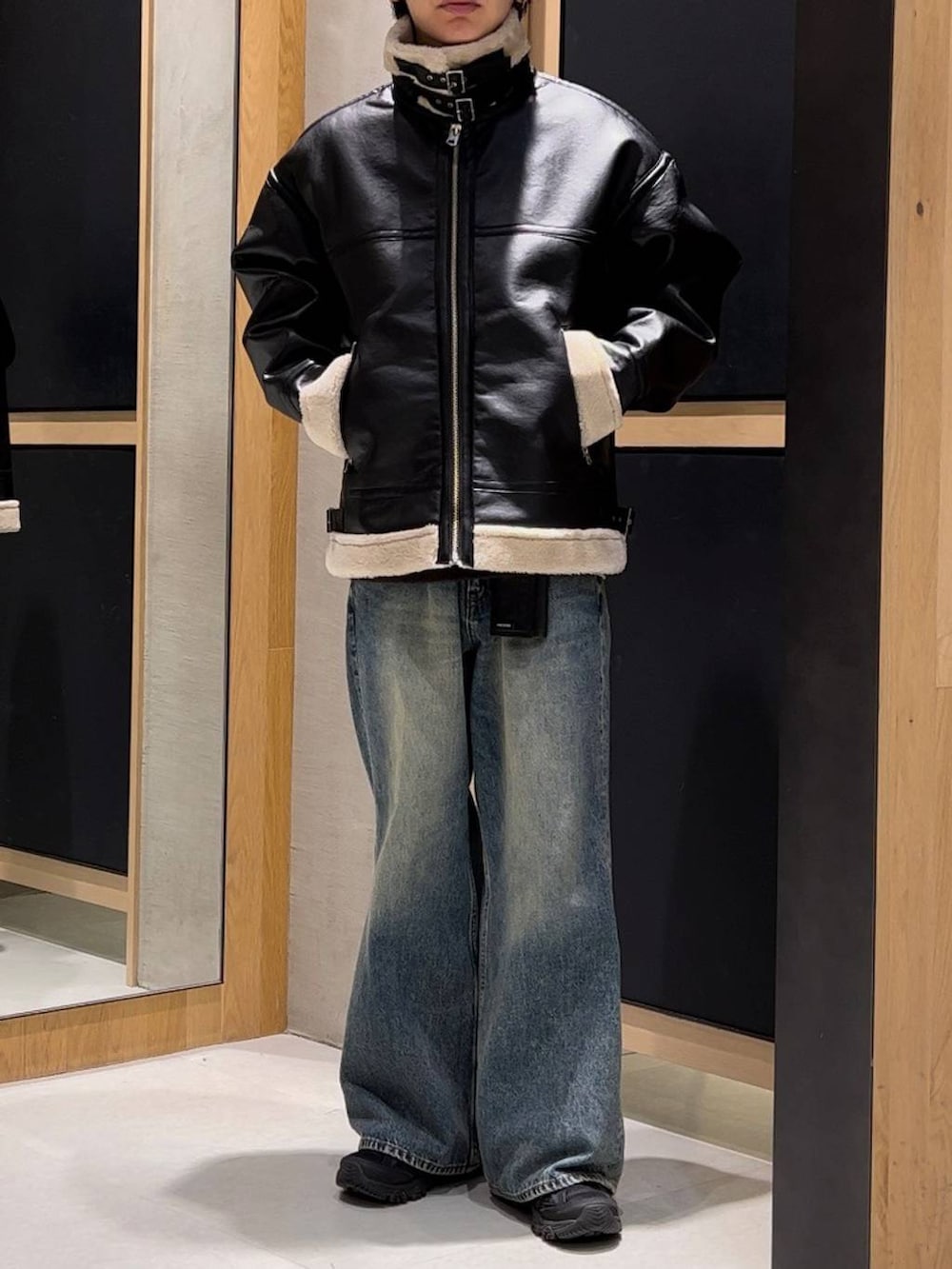 ブラック系のムートンコート、ブラウン系のニット/セーター、ブルー系のデニムパンツを着用したメンズの冬コーディネートの2枚目の写真