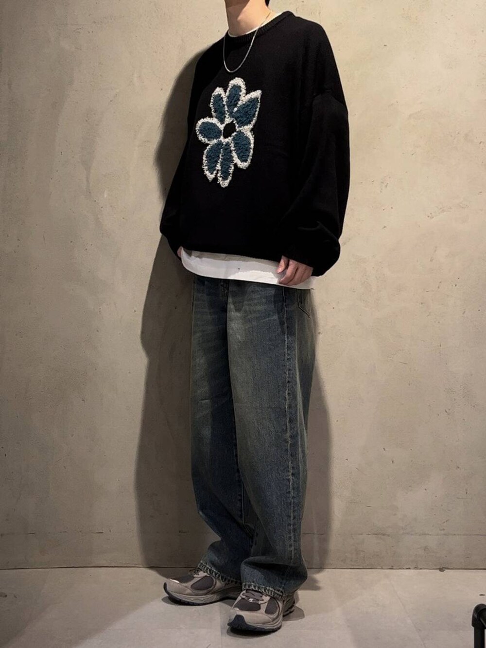 ブルー系のデニムパンツ、ブラック系のニット/セーター、シルバー系のネックレスを着用したメンズの秋コーディネートの2枚目の写真