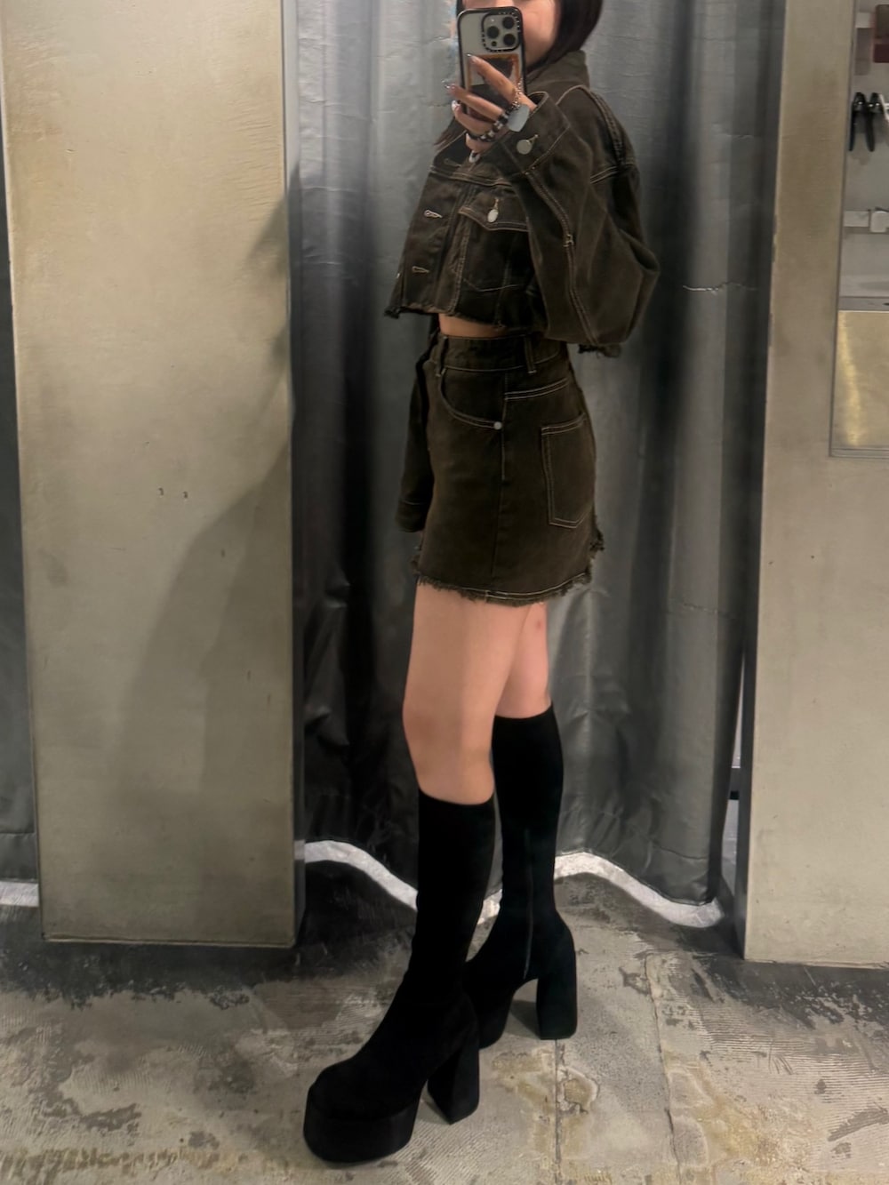 ブラウン系のデニムジャケット、ブラウン系のスカート、ブラック系のブーツを着用したレディースの夏コーディネートの2枚目の写真