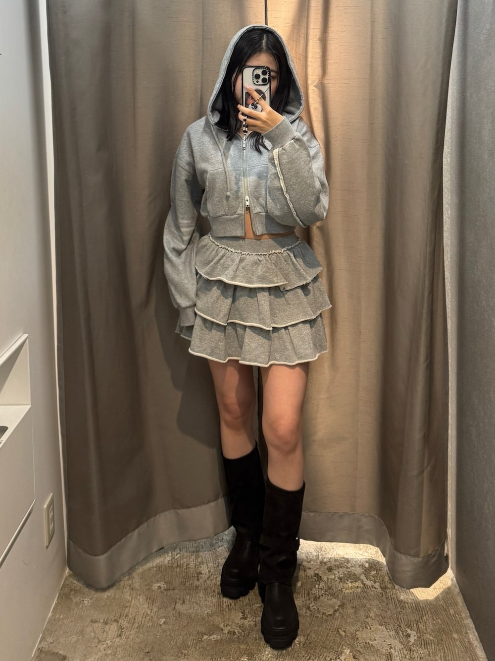 グレー系のパーカー、グレー系のスカート、ブラック系のブーツを着用したレディースの秋コーディネートの2枚目の写真