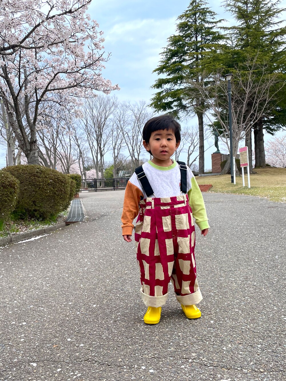 ピンク系のサロペット/オーバーオール、グリーン系のTシャツ/カットソー、イエロー系のレインシューズを着用したキッズの春コーディネートの3枚目の写真