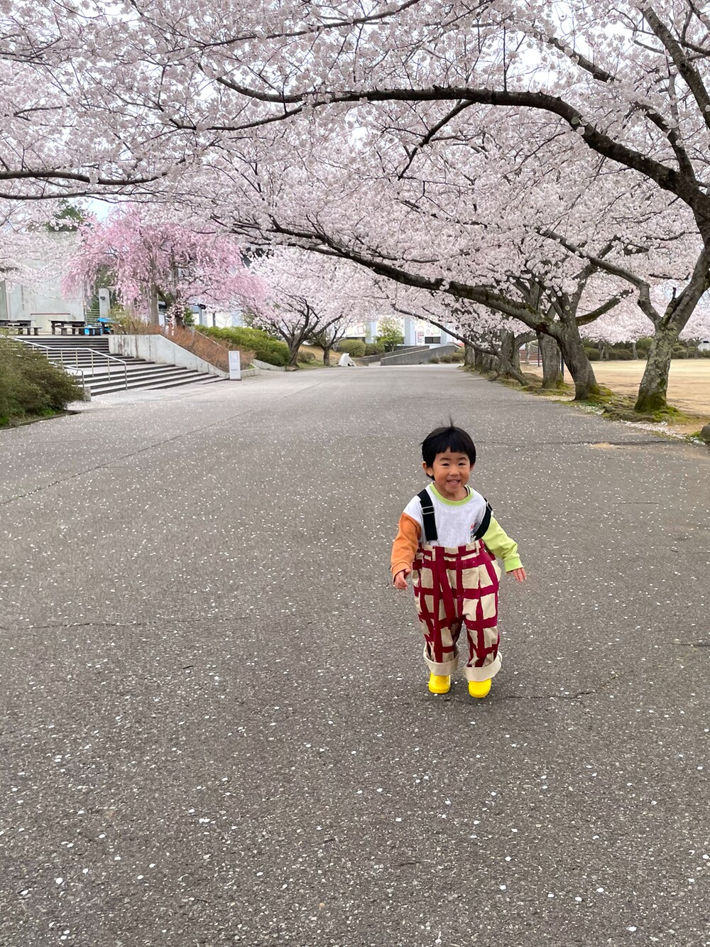 ピンク系のサロペット/オーバーオール、グリーン系のTシャツ/カットソー、イエロー系のレインシューズを着用したキッズの春コーディネートの2枚目の写真