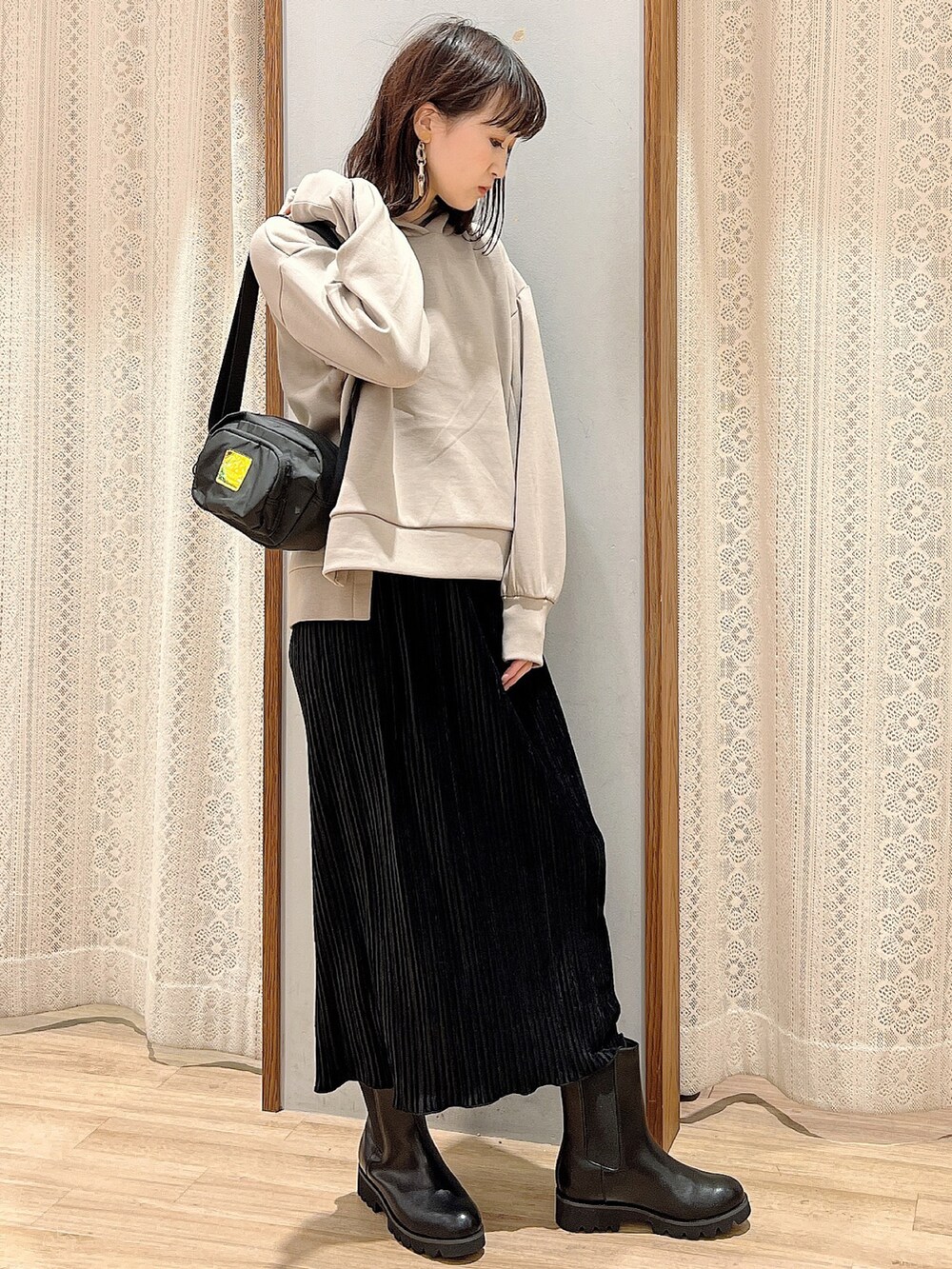 ベージュ系のパーカー、ブラック系のブーツ、ブラック系のショルダーバッグを着用したレディースの秋コーディネートの2枚目の写真