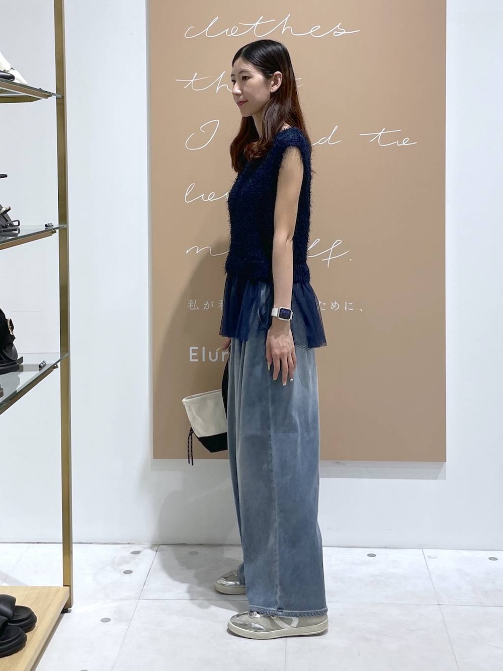 ブルー系のニット/セーター、ブラック系のトートバッグ、ブルー系のデニムパンツを着用したレディースの夏コーディネートの2枚目の写真