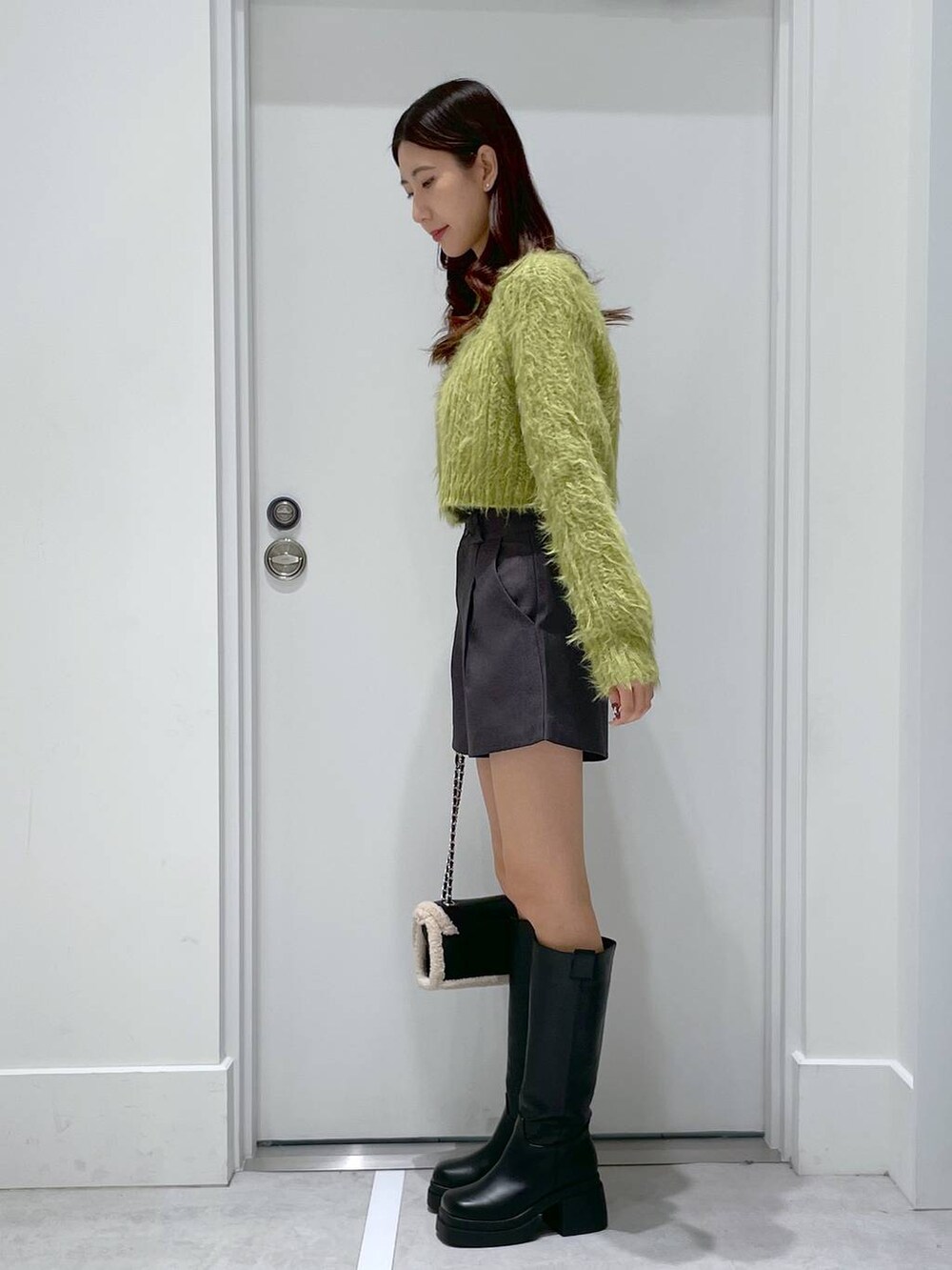 ブラック系のショルダーバッグ、ブラック系のブーツ、グリーン系のニット/セーターを着用したレディースの冬コーディネートの2枚目の写真