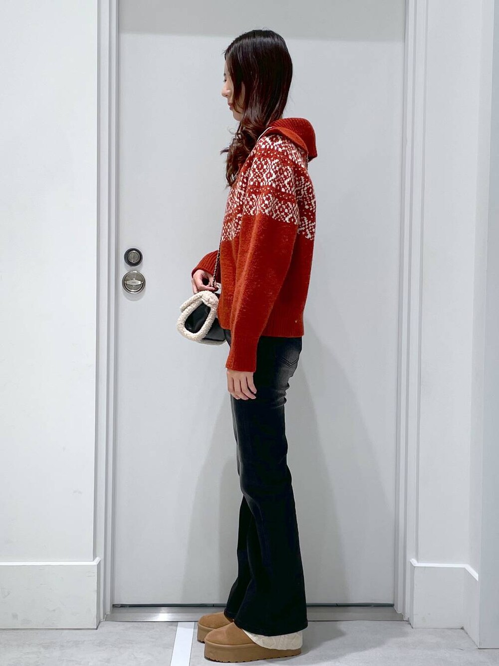 レッド系のニット/セーター、ブラック系のデニムパンツ、ブラック系のショルダーバッグを着用したレディースの冬コーディネートの2枚目の写真