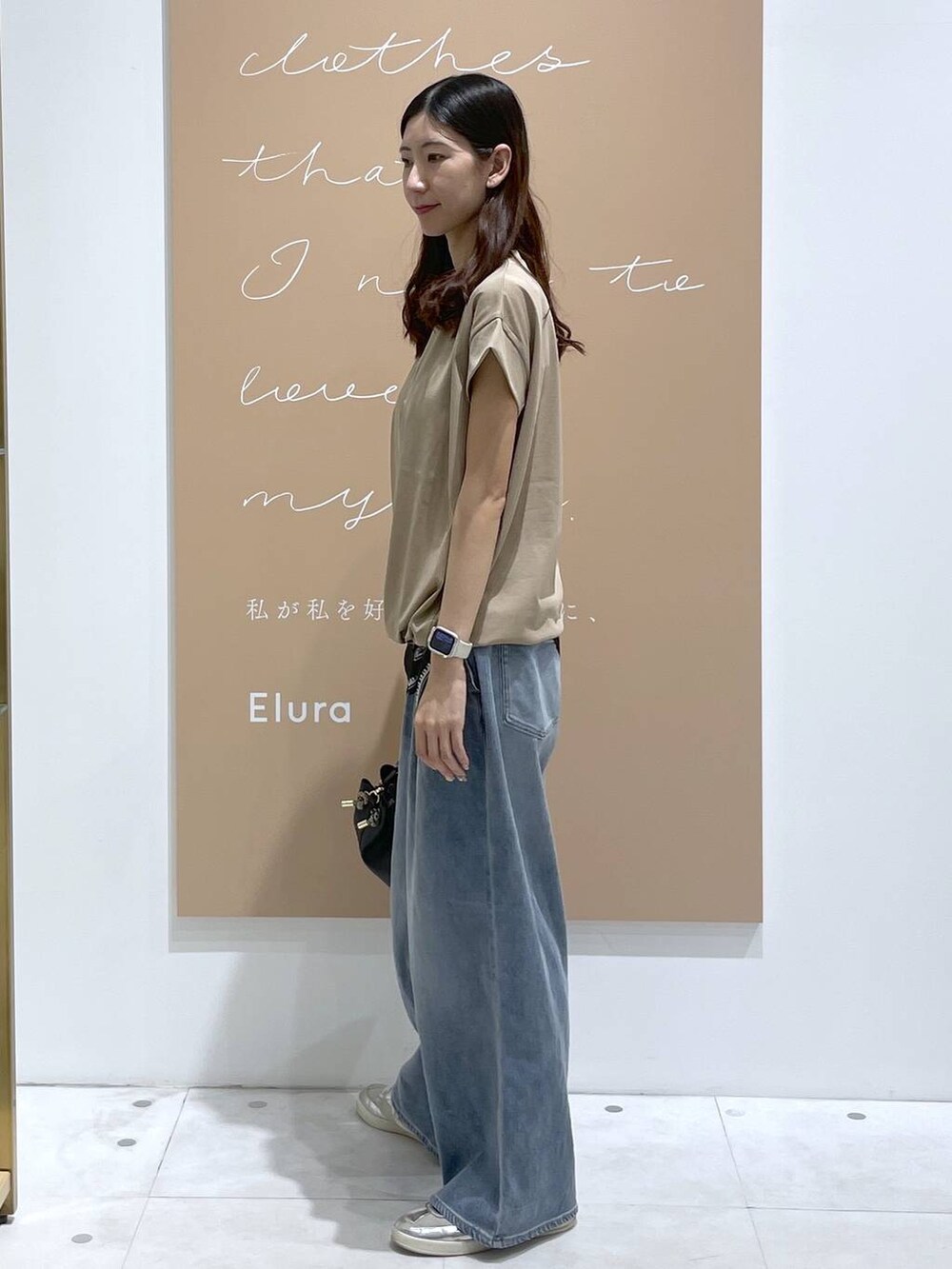 ブラック系のハンドバッグ、ブルー系のデニムパンツ、シルバー系のネックレスを着用したレディースの夏コーディネートの2枚目の写真