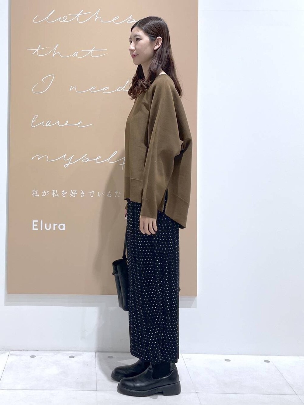 ブラック系のスカート、ブラック系のハンドバッグ、ブラウン系のニット/セーターを着用したレディースの春コーディネートの2枚目の写真