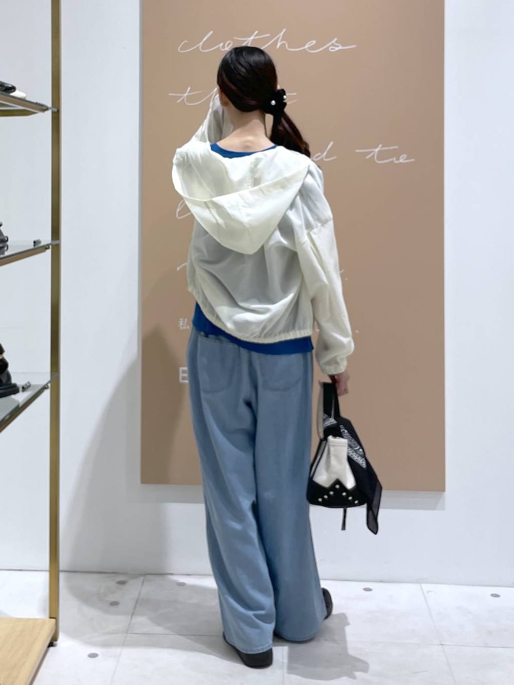ホワイト系のブルゾン、ブルー系のデニムパンツ、ブラック系のトートバッグを着用したレディースの夏コーディネートの3枚目の写真