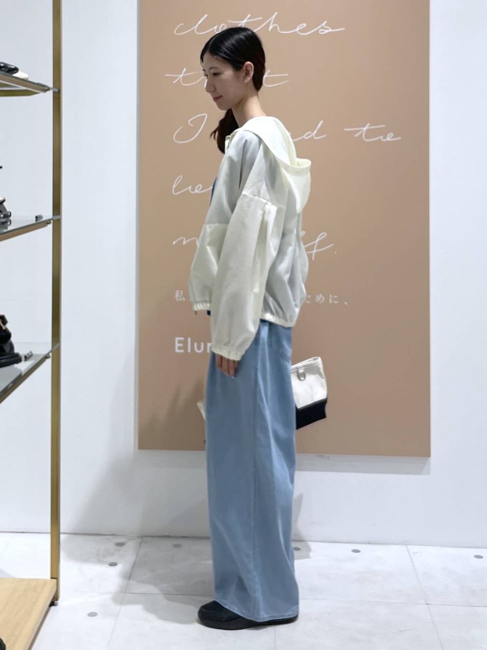 ホワイト系のブルゾン、ブルー系のデニムパンツ、ブラック系のトートバッグを着用したレディースの夏コーディネートの2枚目の写真