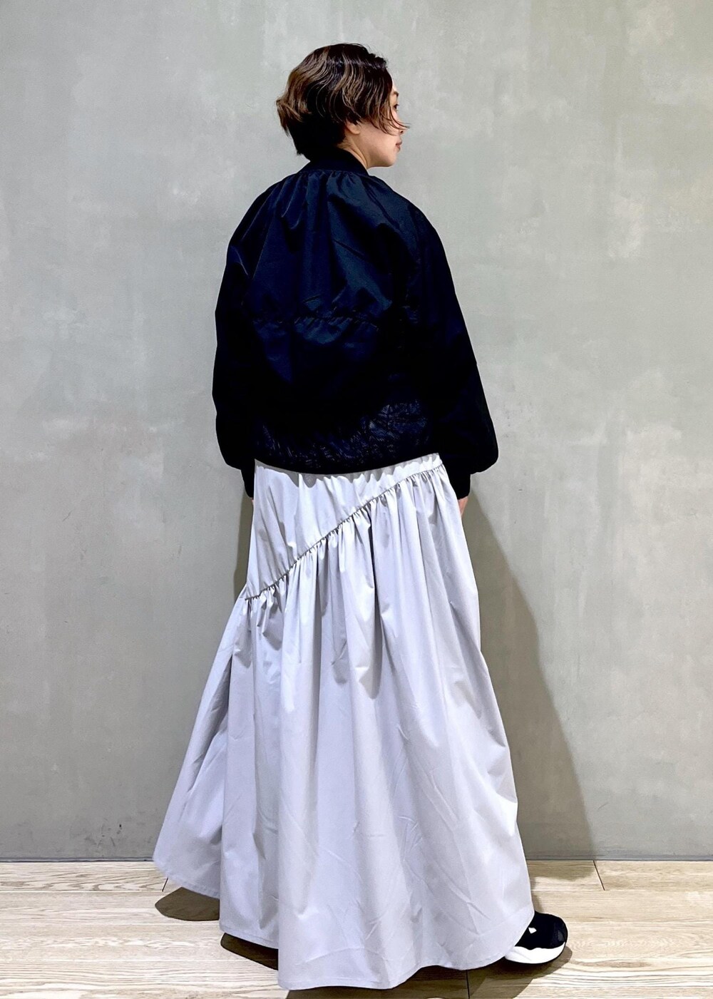 グレー系のワンピース、ブラック系のブルゾン、ブラック系のスニーカーを着用したレディースの春コーディネートの4枚目の写真