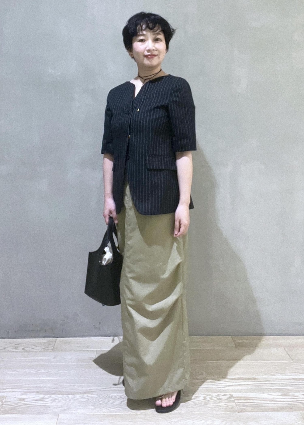 ブラック系のハンドバッグ、ブラック系のノーカラージャケット、ブラック系のサンダルを着用したレディースの夏コーディネートの2枚目の写真