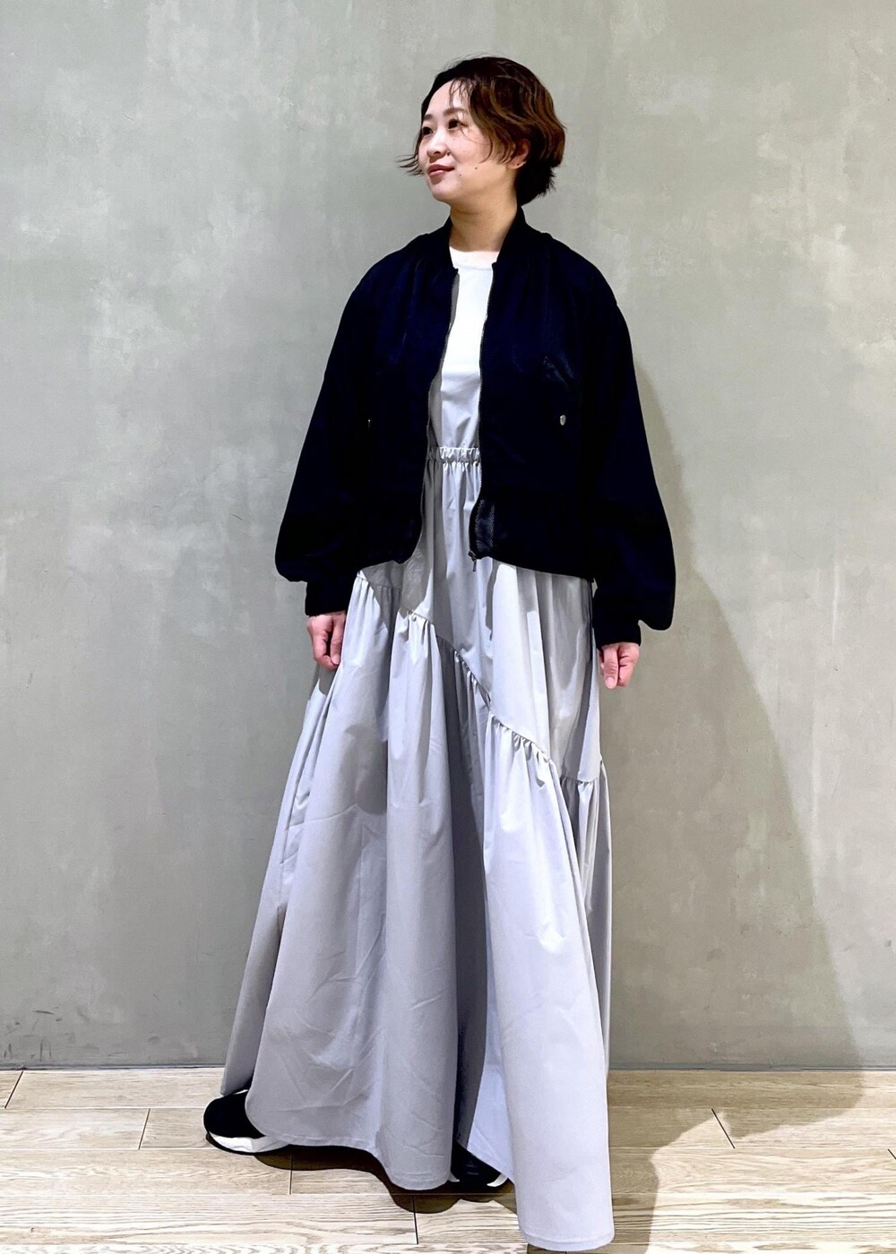 グレー系のワンピース、ブラック系のブルゾン、ブラック系のスニーカーを着用したレディースの春コーディネートの3枚目の写真