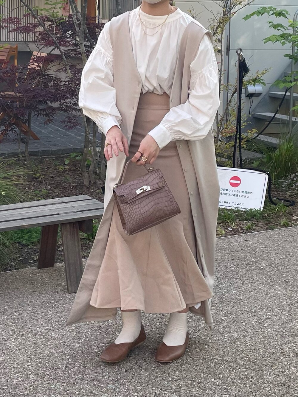 ベージュ系のスカート、ホワイト系のシャツ/ブラウス、ベージュ系のジャンパースカートを着用したレディースの春コーディネートの2枚目の写真