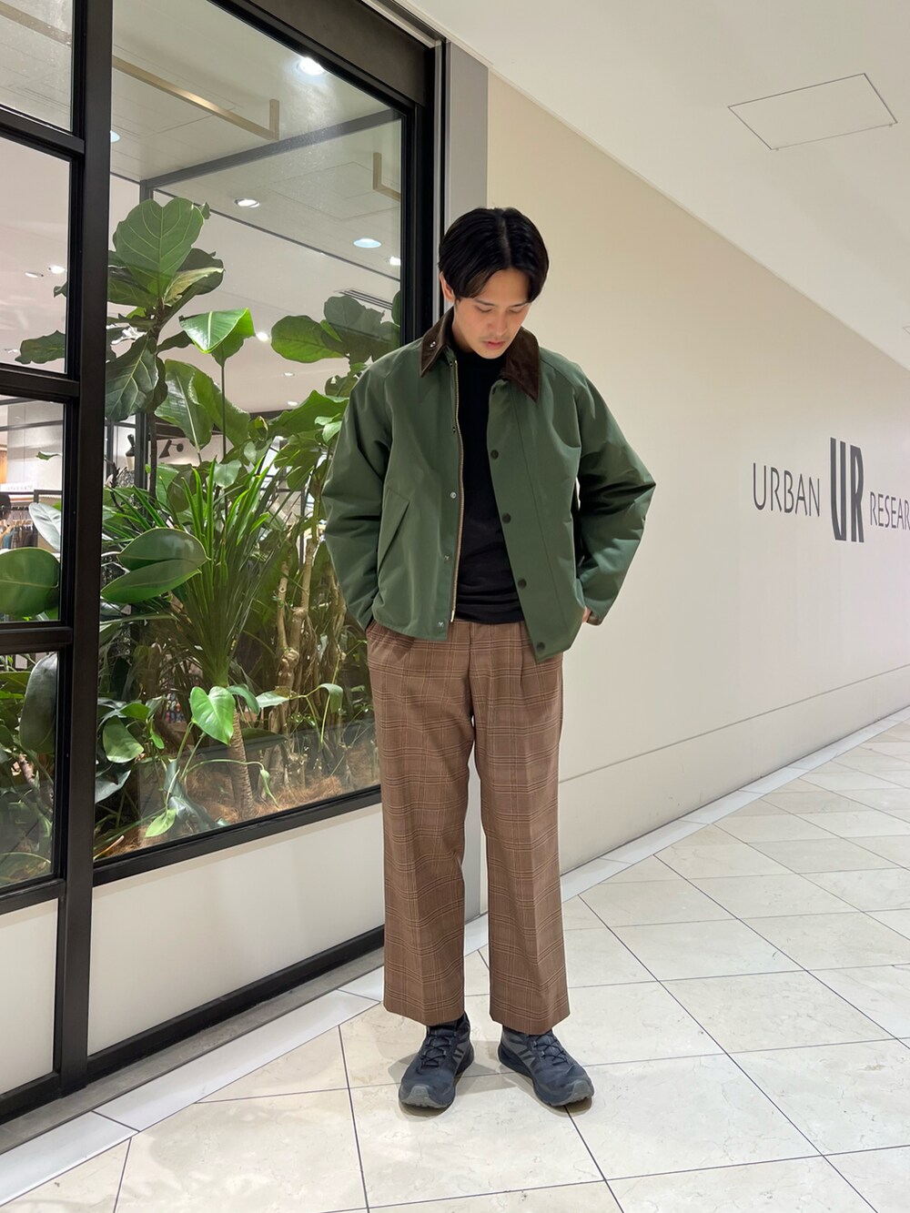 グリーン系のナイロンジャケット、ブラウン系のパンツ、グレー系のスニーカーを着用したメンズの秋コーディネートの2枚目の写真