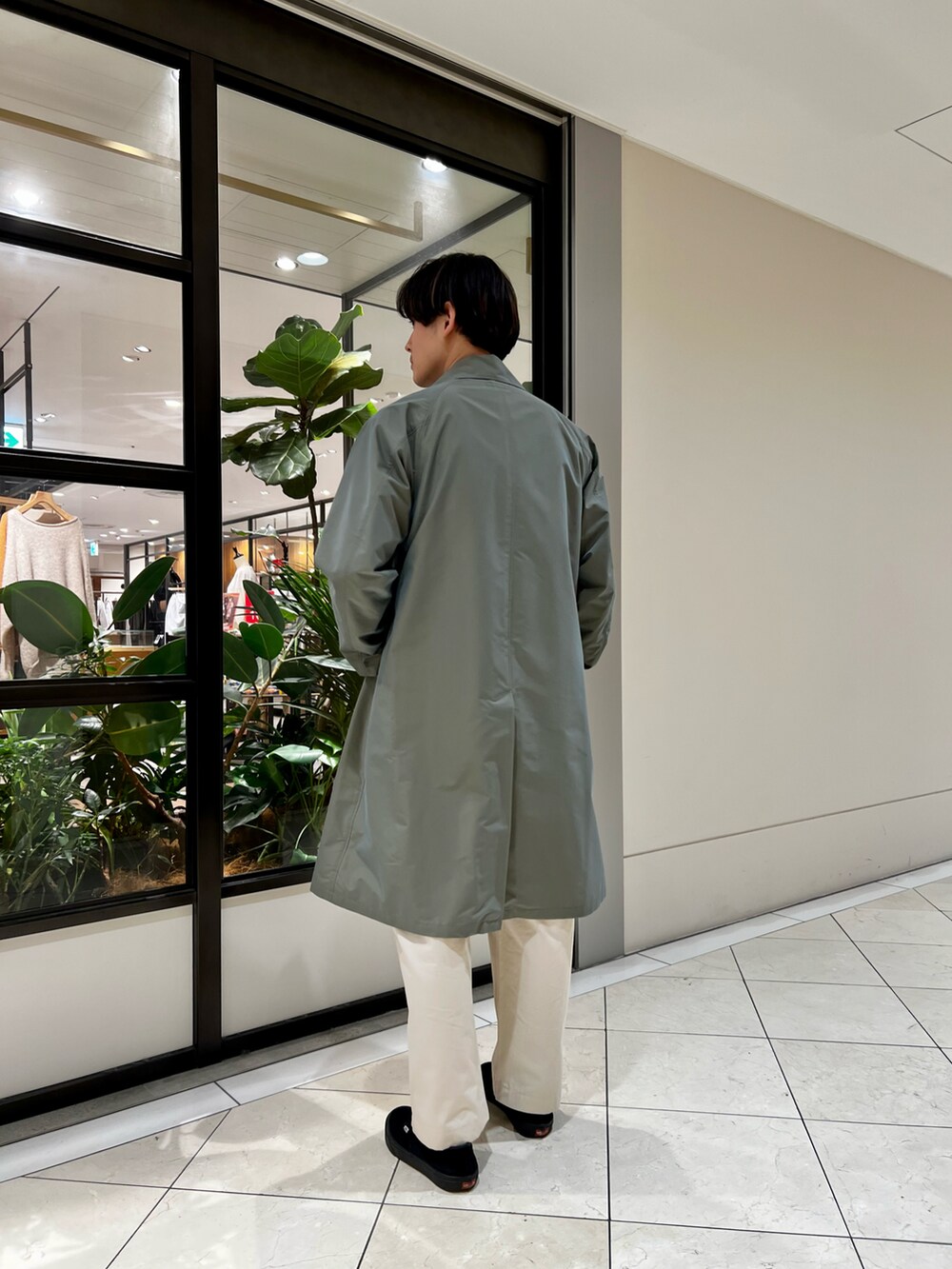 グリーン系のトレンチコート、レッド系のTシャツ/カットソー、ホワイト系のチノパンツを着用したメンズの冬コーディネートの2枚目の写真