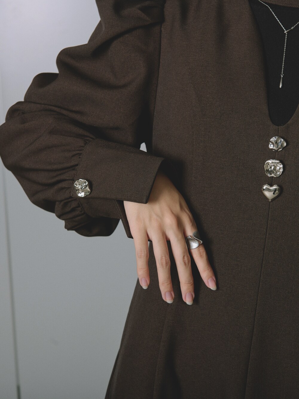 ブラック系のクラッチバッグ、ブラウン系のワンピース、シルバー系のイヤリングを着用したレディースの冬コーディネートの2枚目の写真