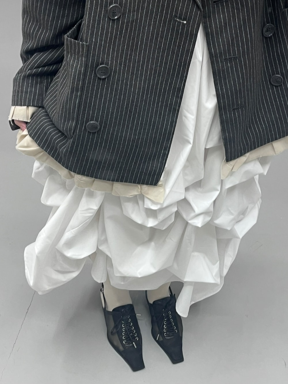 ブラック系のパンプス、ホワイト系のスカート、グレー系のテーラードジャケットを着用したレディースの春コーディネートの2枚目の写真