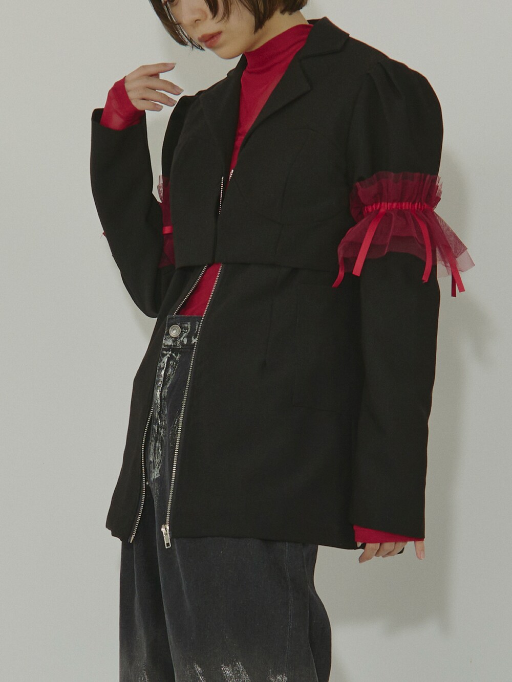 ブラック系のテーラードジャケット、レッド系のトップス、ブラック系のデニムパンツを着用したレディースの冬コーディネートの3枚目の写真