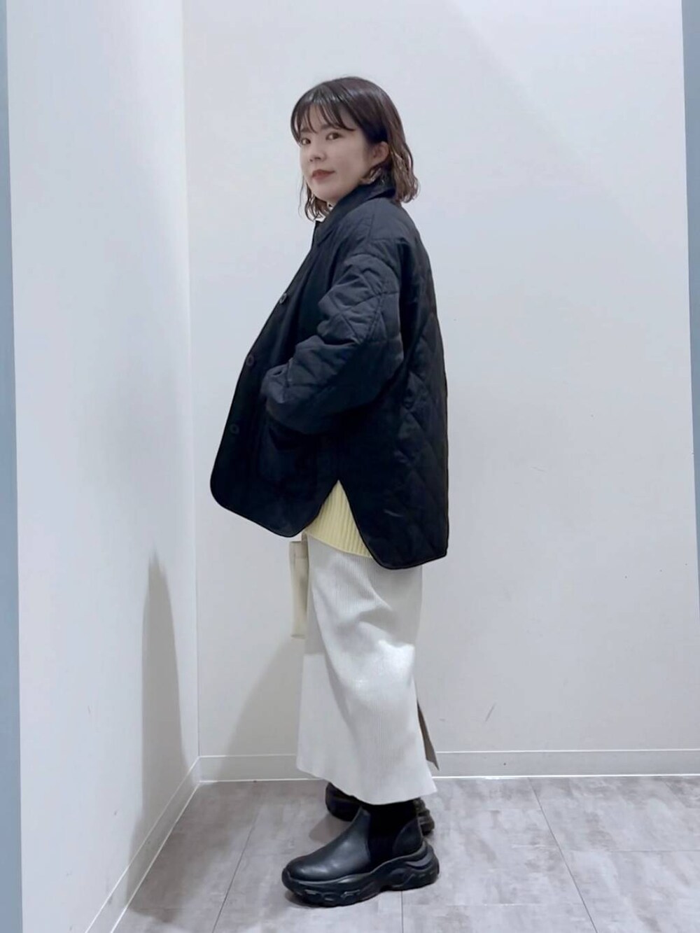 イエロー系のニット/セーター、ホワイト系のショルダーバッグ、ブラック系のブーツを着用したレディースの冬コーディネートの2枚目の写真