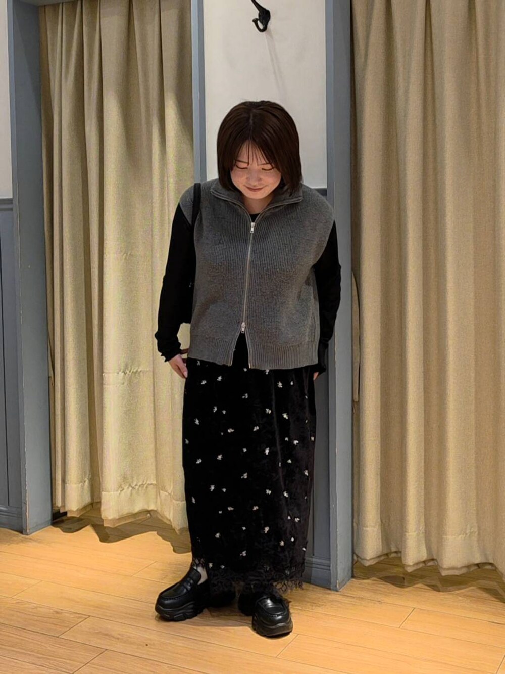 グレー系のベスト、ブラック系のスカート、ブラック系のTシャツ/カットソーを着用したレディースの秋コーディネートの2枚目の写真