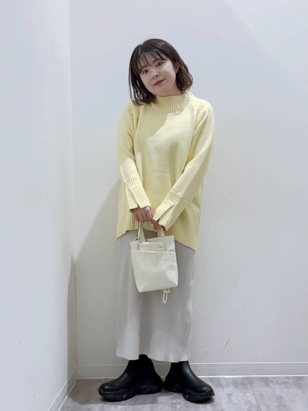 イエロー系のニット/セーター、ホワイト系のショルダーバッグ、ブラック系のブーツを着用したレディースの冬コーディネートの4枚目の写真
