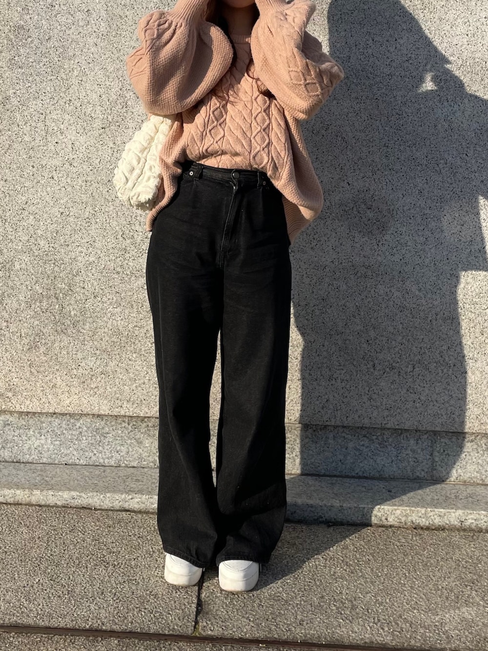 ブラック系のデニムパンツ、ピンク系のニット/セーター、ホワイト系のスニーカーを着用したレディースの春コーディネートの2枚目の写真