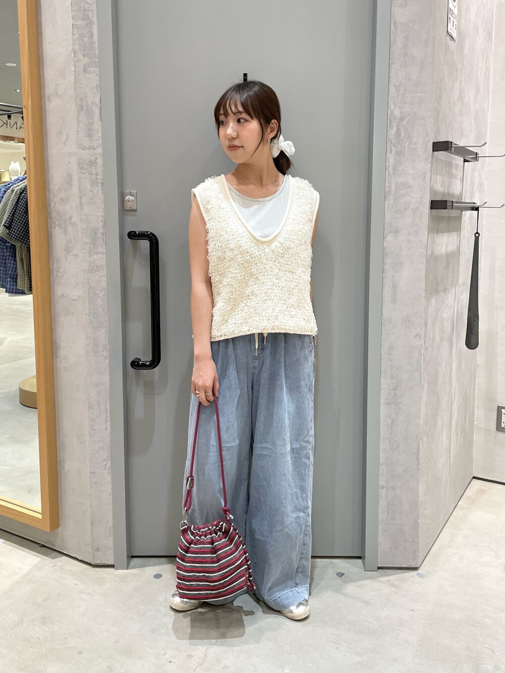 ホワイト系のベスト、ブルー系のデニムパンツ、レッド系のショルダーバッグを着用したレディースの夏コーディネートの2枚目の写真