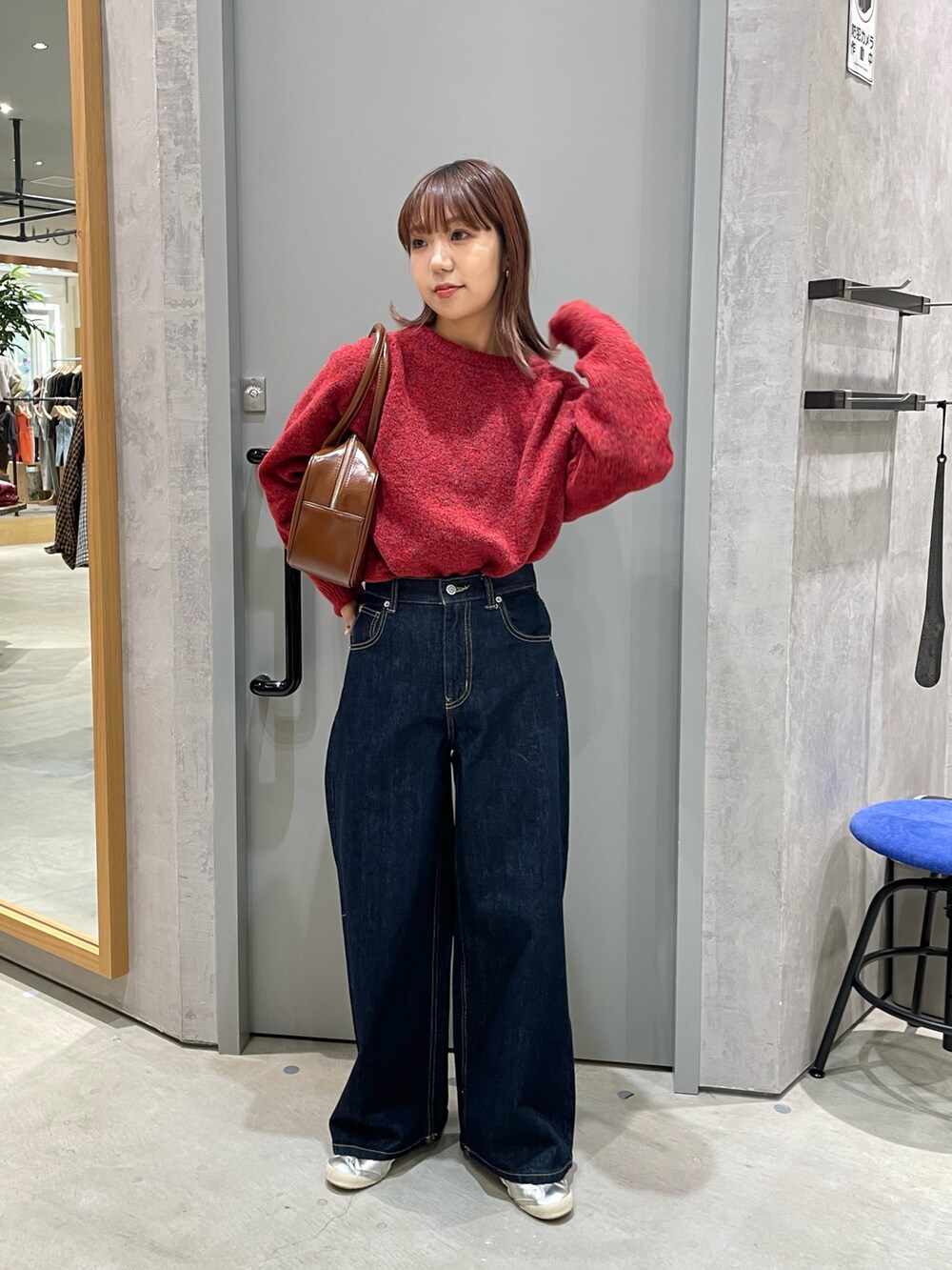 レッド系のニット/セーター、ブラウン系のボストンバッグ、ブルー系のデニムパンツを着用したレディースの秋コーディネートの2枚目の写真