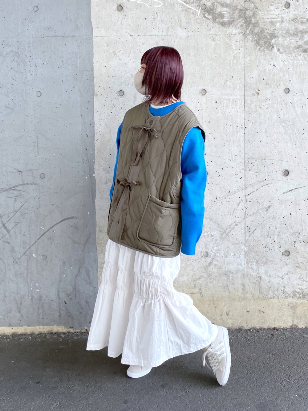 グリーン系のベスト、ホワイト系のスカート、ホワイト系のスニーカーを着用したレディースの冬コーディネートの2枚目の写真