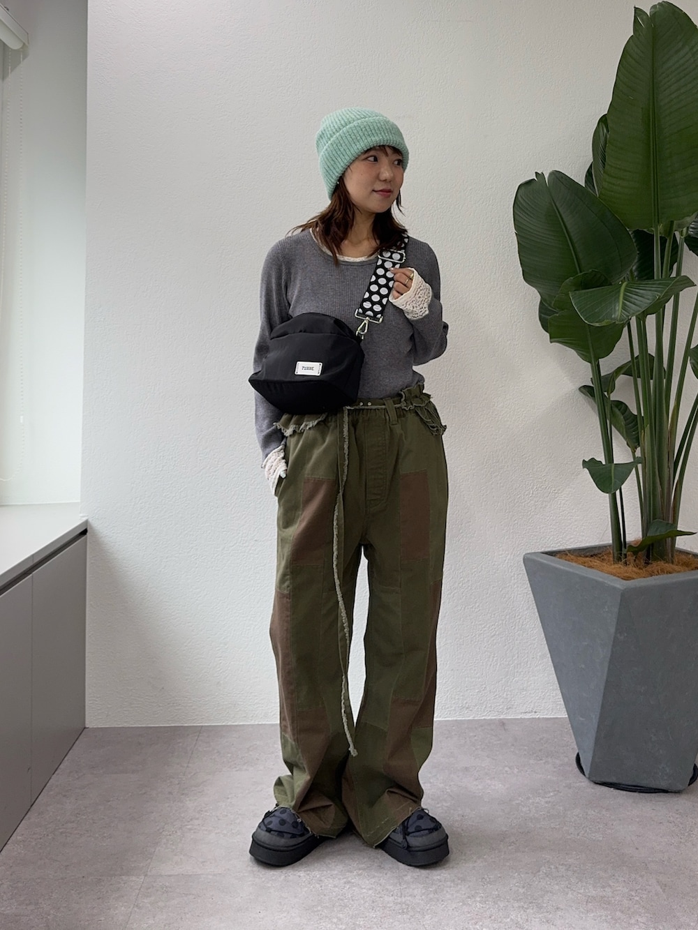 グリーン系のその他パンツ、グレー系のその他シューズ、ブラック系のショルダーバッグを着用したレディースの秋コーディネートの2枚目の写真
