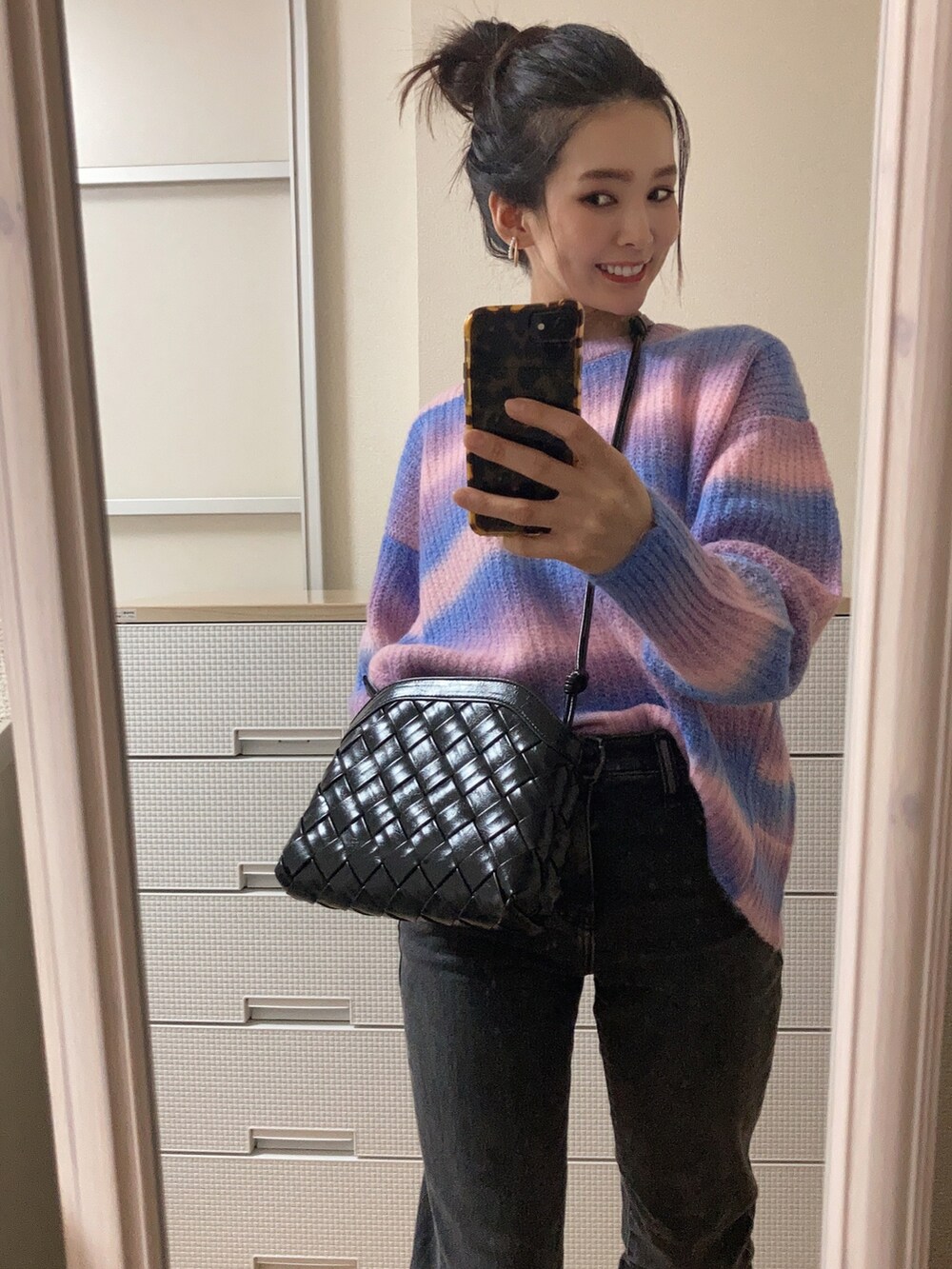 パープル系のニット/セーター、ブラック系のショルダーバッグ、ブラック系のデニムパンツを着用したレディースの秋コーディネートの2枚目の写真