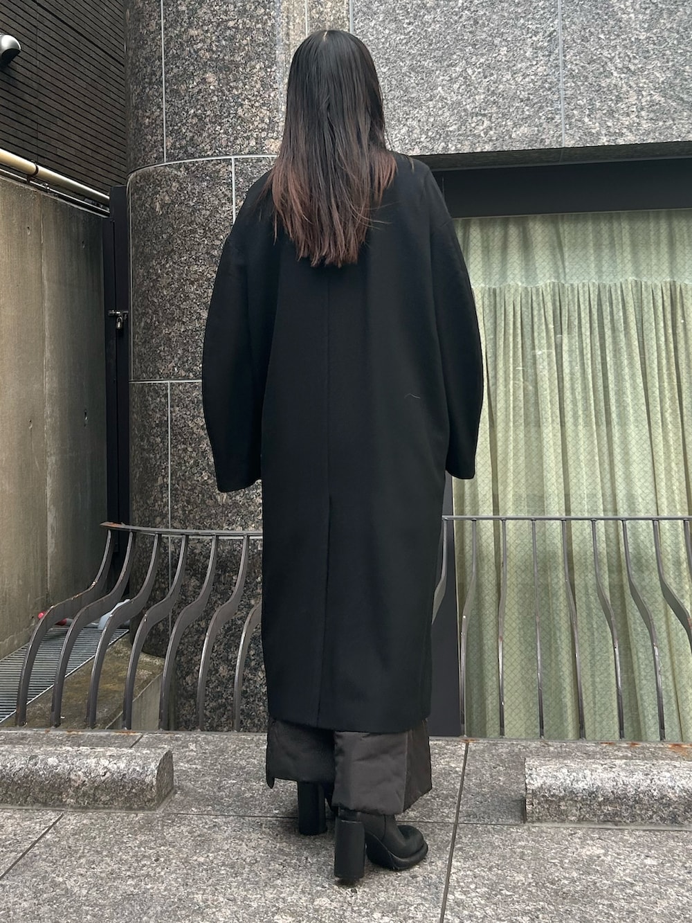 ブラック系のステンカラーコート、ブラック系のブーツを着用したレディースの秋コーディネートの3枚目の写真