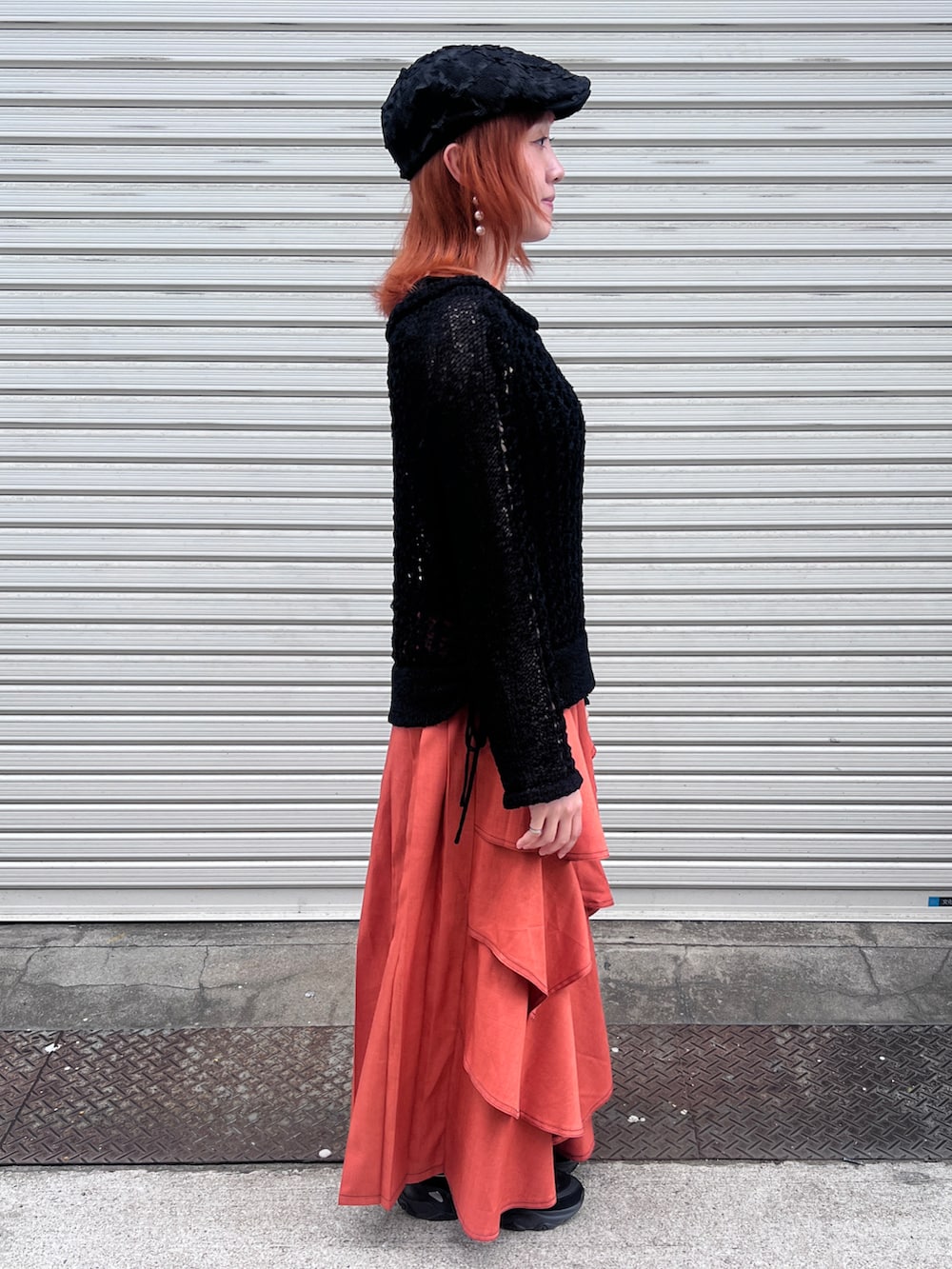 ブラック系のニット/セーター、オレンジ系のスカート、ブラック系のハンチング/ベレー帽を着用したレディースの夏コーディネートの3枚目の写真