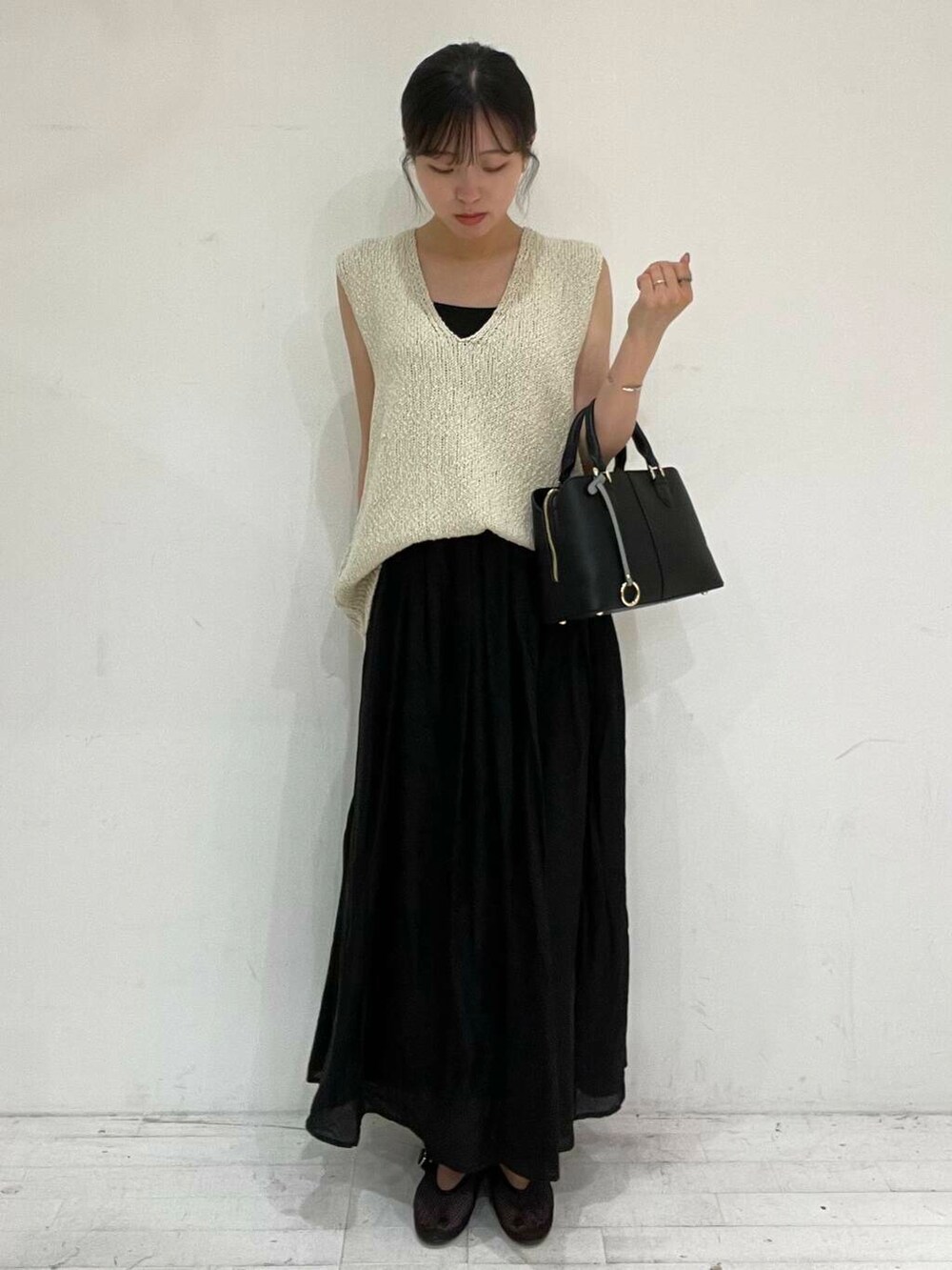 ブラック系のハンドバッグ、ブラック系のバレエシューズ、ベージュ系のベストを着用したレディースの夏コーディネートの2枚目の写真