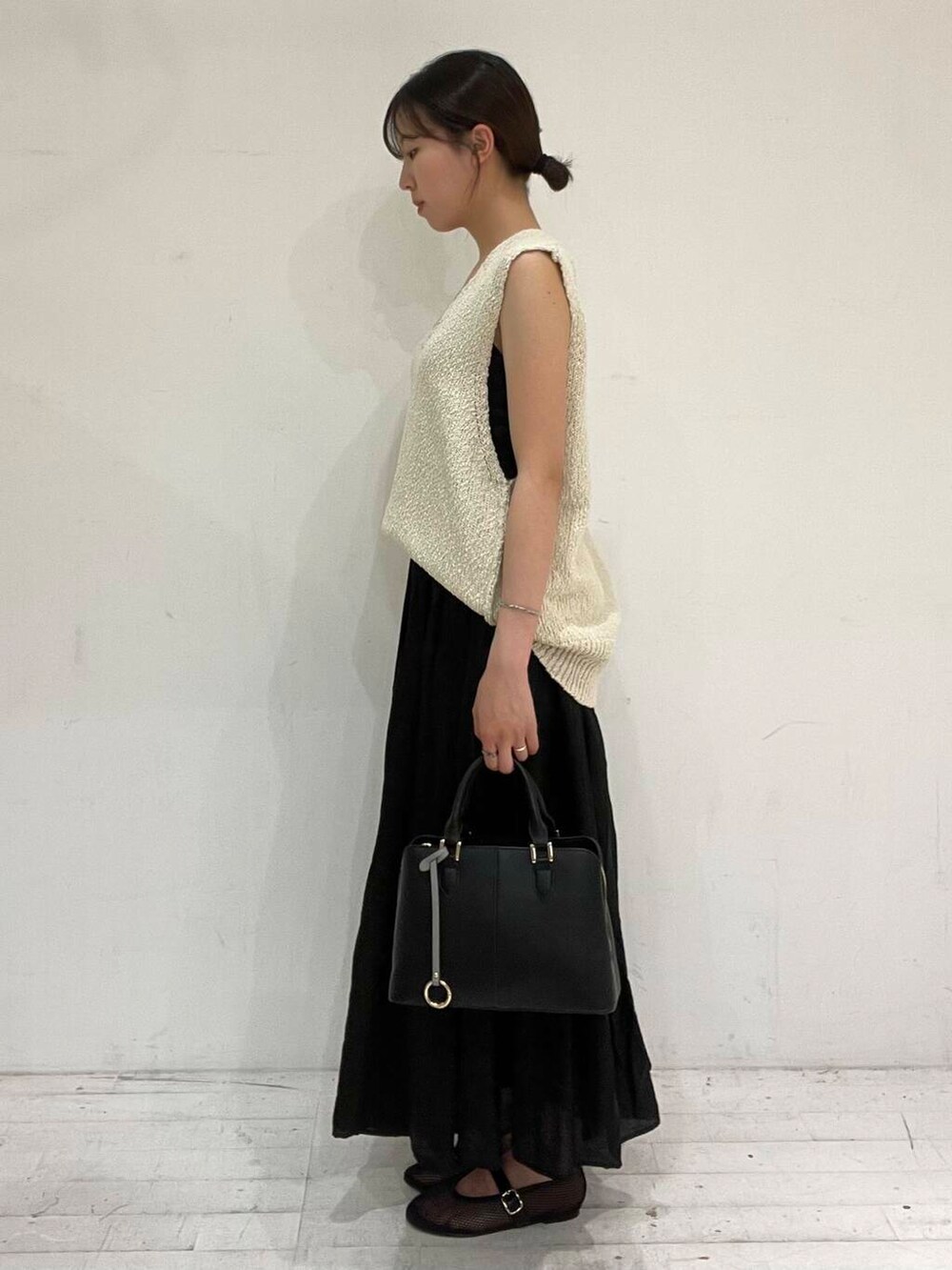 ブラック系のハンドバッグ、ブラック系のバレエシューズ、ベージュ系のベストを着用したレディースの夏コーディネートの3枚目の写真
