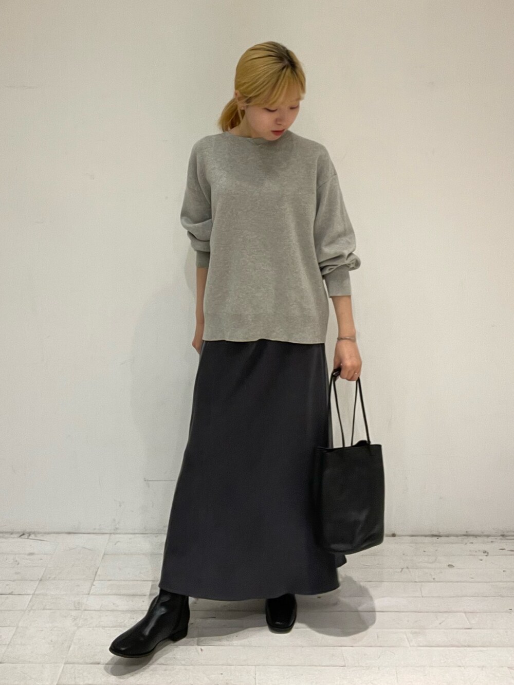 グレー系のスカート、ブラック系のブーツ、ブラック系のショルダーバッグを着用したレディースの秋コーディネートの2枚目の写真